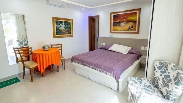 Ein Schlafzimmer mit einem Bett, einem Sessel, einem Tisch mit Pflanze und zwei Bildern an der Wand.