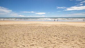 Ein weiter Sandstrand mit blauem Himmel und ruhigen Wellen.