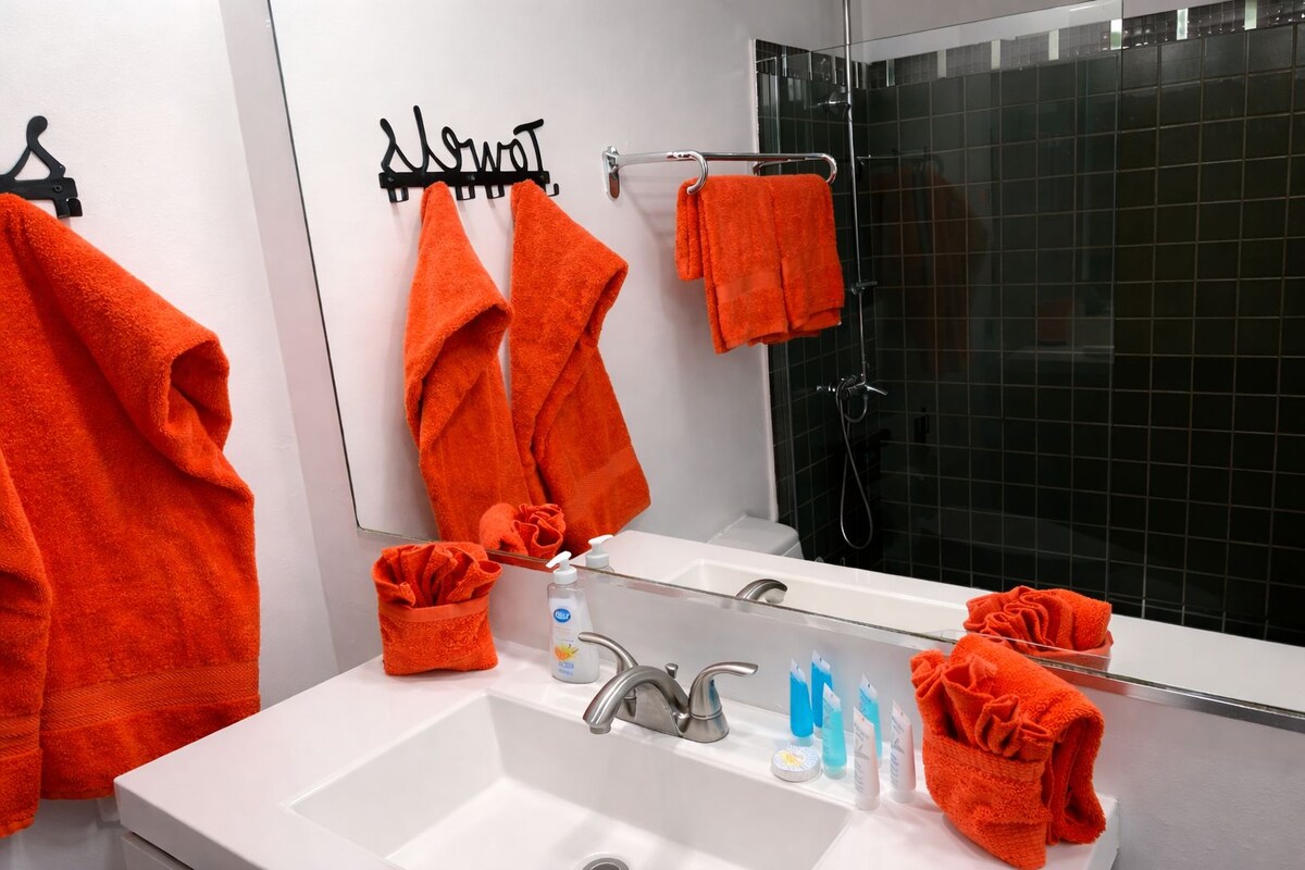 A bathroom with a white sink, a mirror, and two orange towels hanging on a black towel rack.