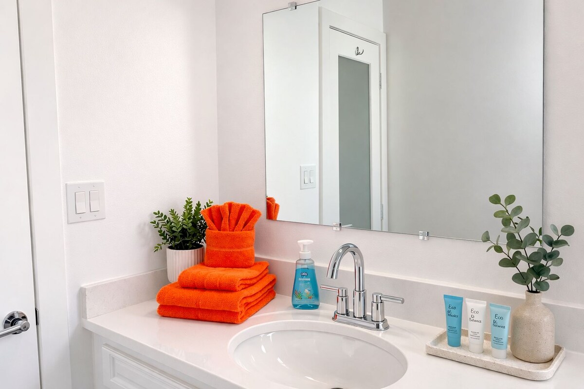 A bathroom with a white sink, a mirror, a towel rack, a potted plant, and toiletries.