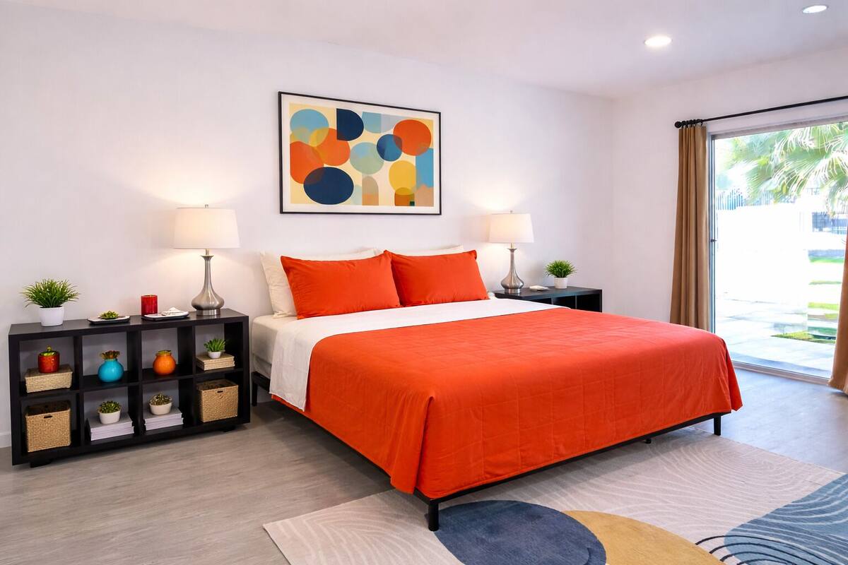Une chambre moderne avec un lit, deux tables de chevet, une commode, une œuvre d’art murale et une vue sur l’extérieur.