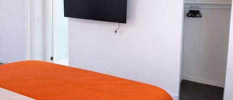 A bedroom with a bed, a television mounted on the wall, and a walk-in closet with hanging clothes.