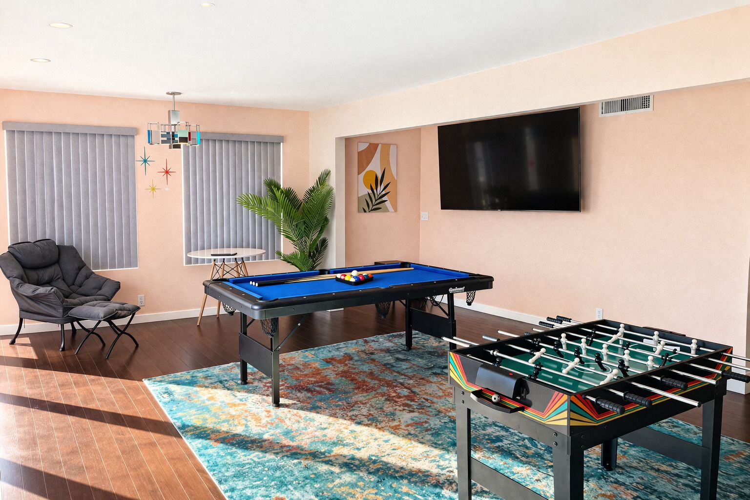 Une pièce équipée d’une table de billard, d’un baby-foot, d’un fauteuil confortable, d’un téléviseur et d’une plante.