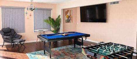 Une pièce équipée d’une table de billard, d’un baby-foot, d’un fauteuil confortable, d’un téléviseur et d’une plante.