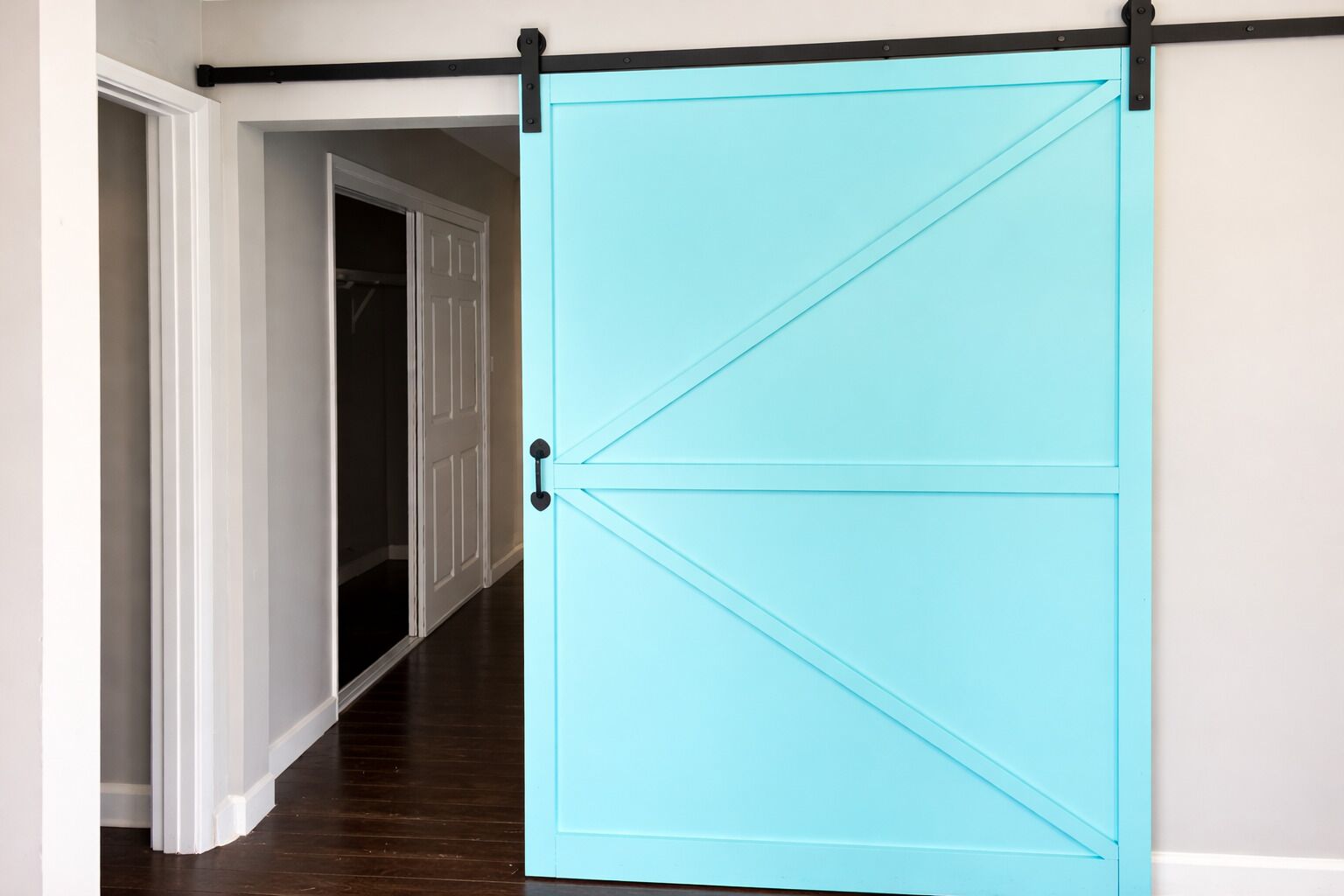 A light blue sliding barn door in a hallway with a white door and dark wooden flooring.
