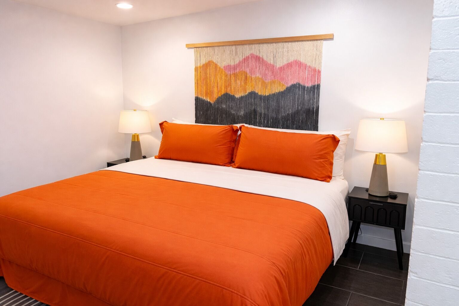 Ein Hotelzimmer mit einem großen Bett, zwei Nachttischen mit Lampen, einem Wandteppich und einer weißen Ziegelwand.