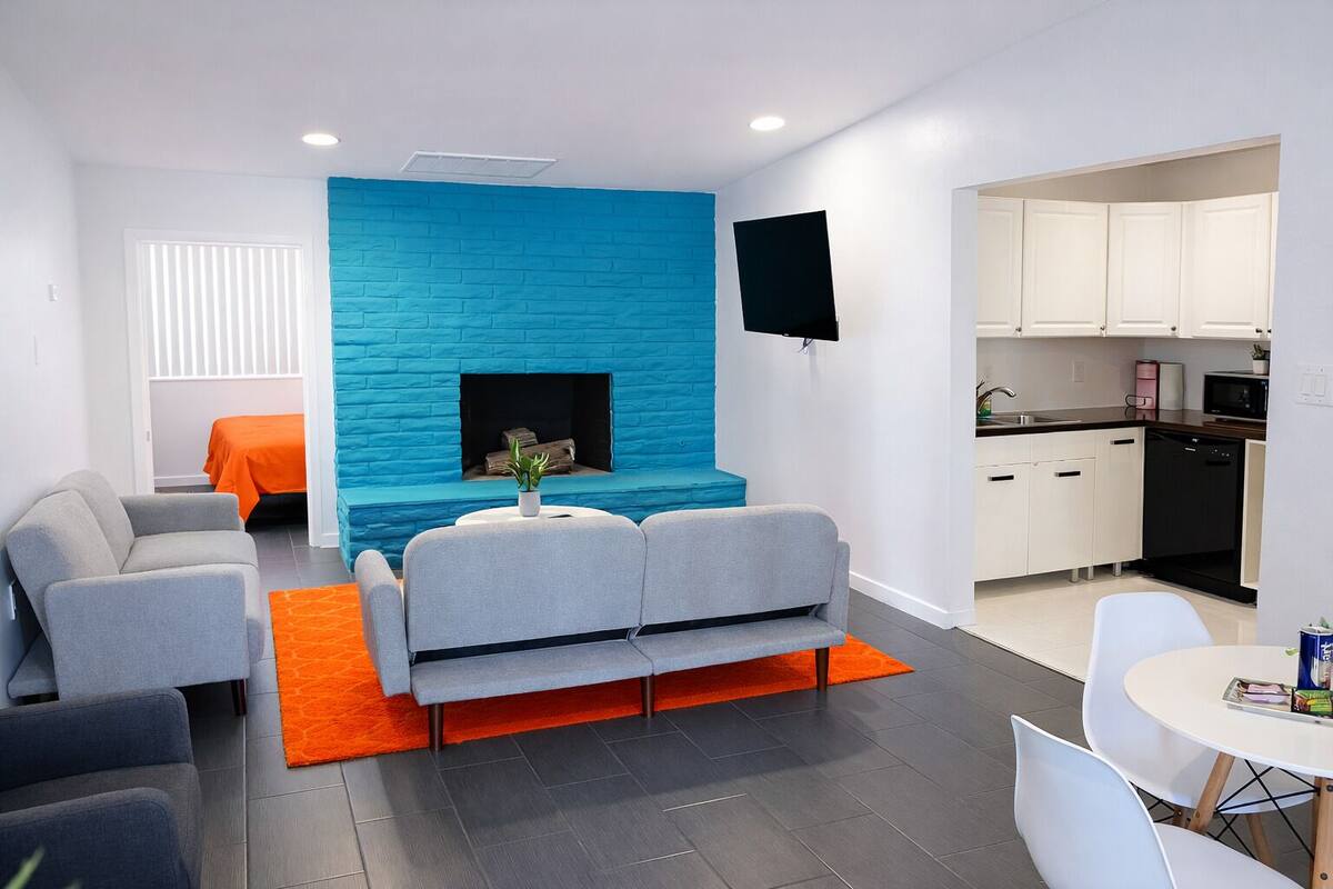 Un salon moderne avec un mur d’accent bleu, des canapés gris, un téléviseur à écran plat et un coin cuisine doté de meubles blancs.