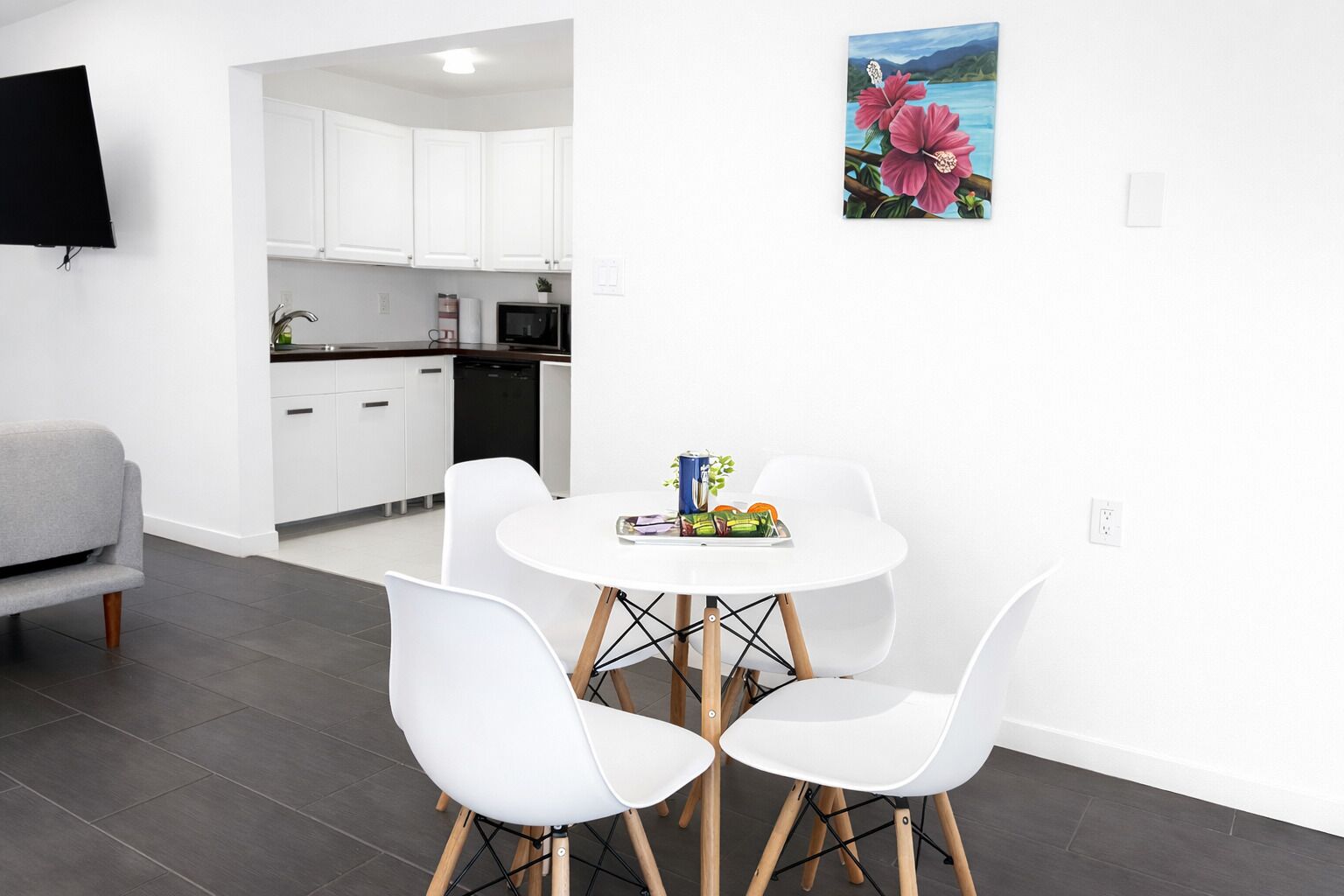 Una cocina moderna con armarios blancos, una mesa de comedor con cuatro sillas y un televisor de pantalla plana montado en la pared.