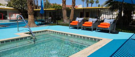 A swimming pool with lounge chairs and umbrellas, surrounded by palm trees and a fence.