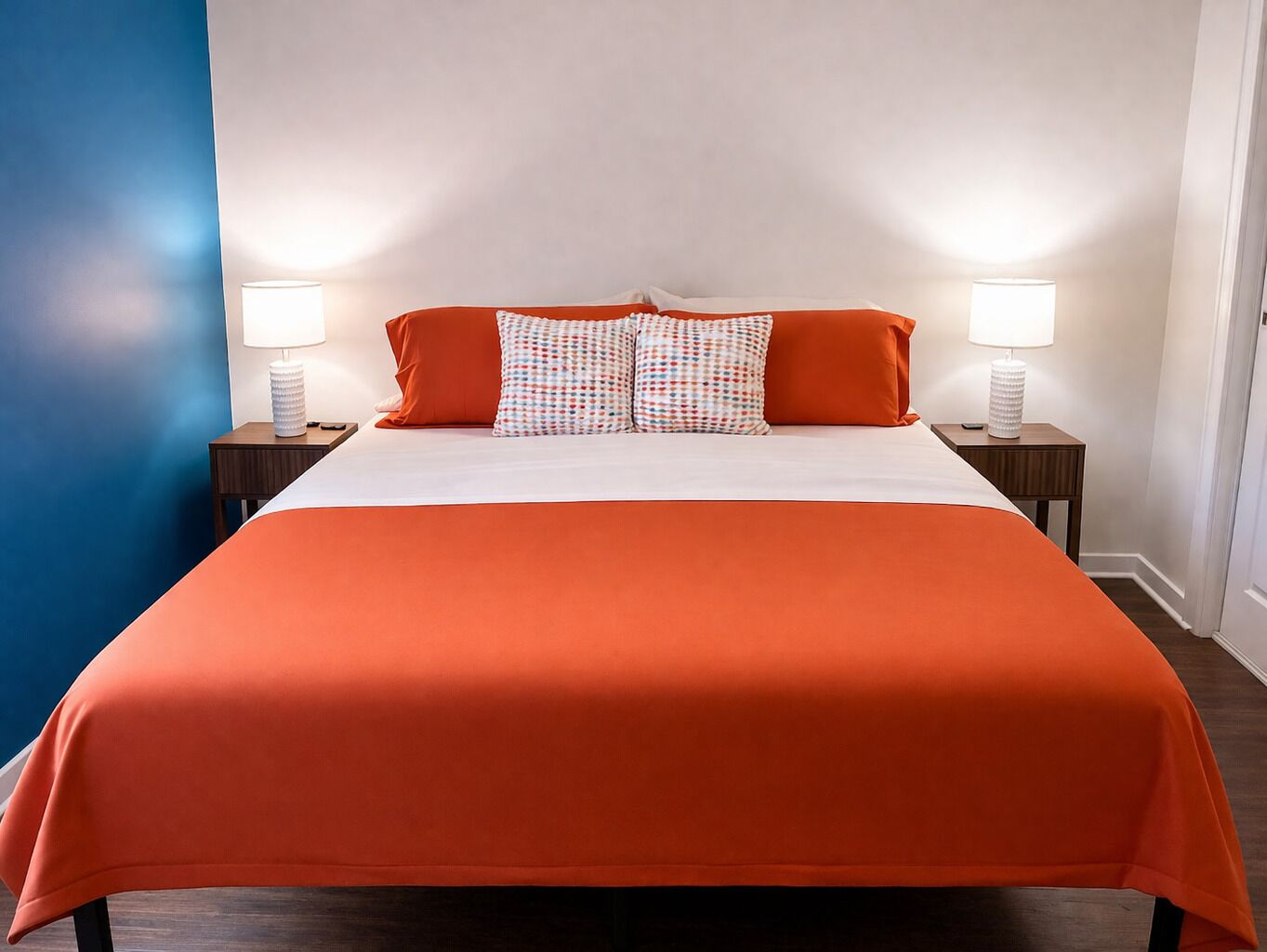 A bed with a white and orange bedspread, two matching pillows, and two bedside lamps on wooden nightstands.