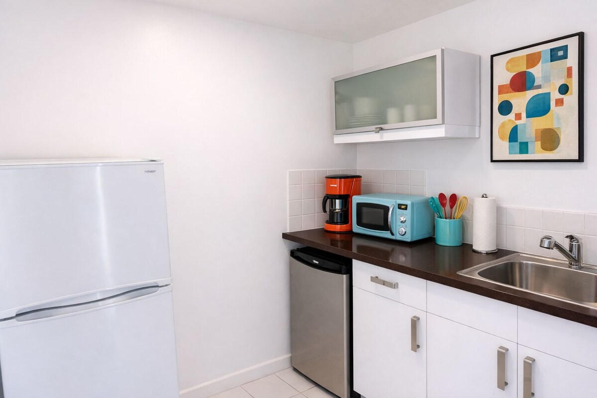 A compact kitchen with a white refrigerator, a coffee maker, a microwave, and a sink.