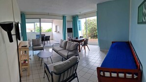 Ein Zimmer mit einer Couch, Sesseln, einem kleinen Tisch, einem Bett und einem Balkon mit Tisch und Stühlen.
