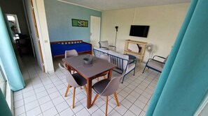 A room with a dining table, chairs, a sofa, a TV, and a fan.