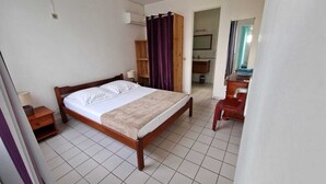 Ein Schlafzimmer mit einem hölzernen Bett, einem Nachttisch, einem Schreibtisch mit Stuhl und einem durch eine offene Tür einsehbaren Badezimmer.