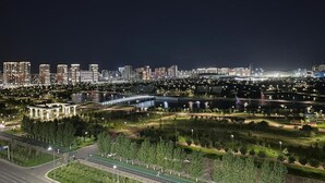 Eine beleuchtete Stadtlandschaft bei Nacht mit Gebäuden, einem Fluss und einem Park mit Wegen.