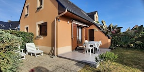 A two-story building with a tiled patio, a table with chairs, and a white lounge chair.