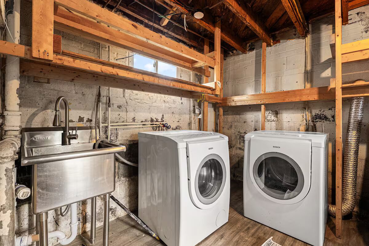 A laundry area with two Bosch washing machines, a stainless steel sink, and wooden beams.
