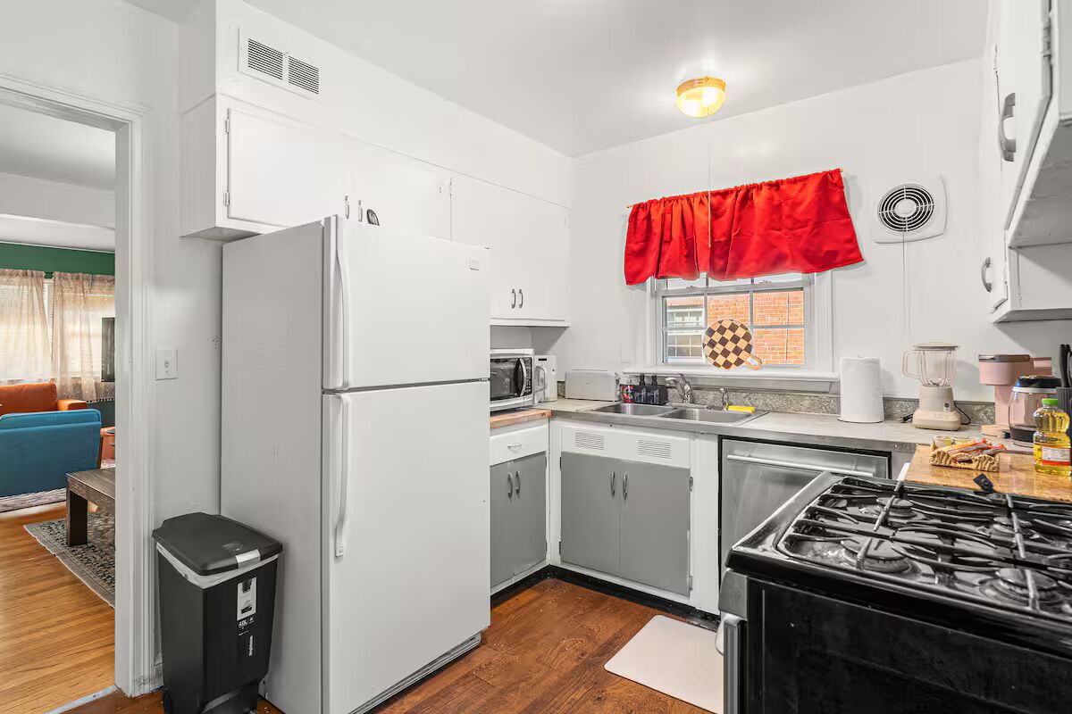Una cocina pequeña con gabinetes blancos, una estufa negra y un frente de ventana rojo.