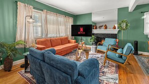 Un salon comprenant un canapé, des fauteuils, une table basse et un téléviseur à écran plat affichant le logo de Netflix.