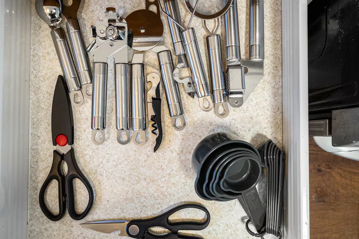 A drawer with various kitchen utensils and tools, including scissors, a corkscrew, and a bottle opener.