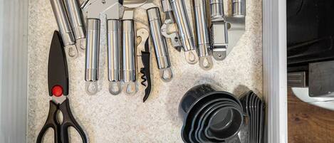 A drawer with various kitchen utensils and tools, including scissors, a corkscrew, and a bottle opener.