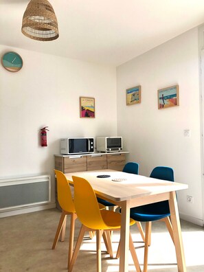 Un espace repas comprenant une table, des chaises, un luminaire suspendu et des appareils fixés au mur.