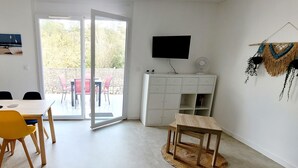 Et værelse med et spisebord, stole, et fjernsyn, et hvidt skab og en skydedør til et udendørs område.