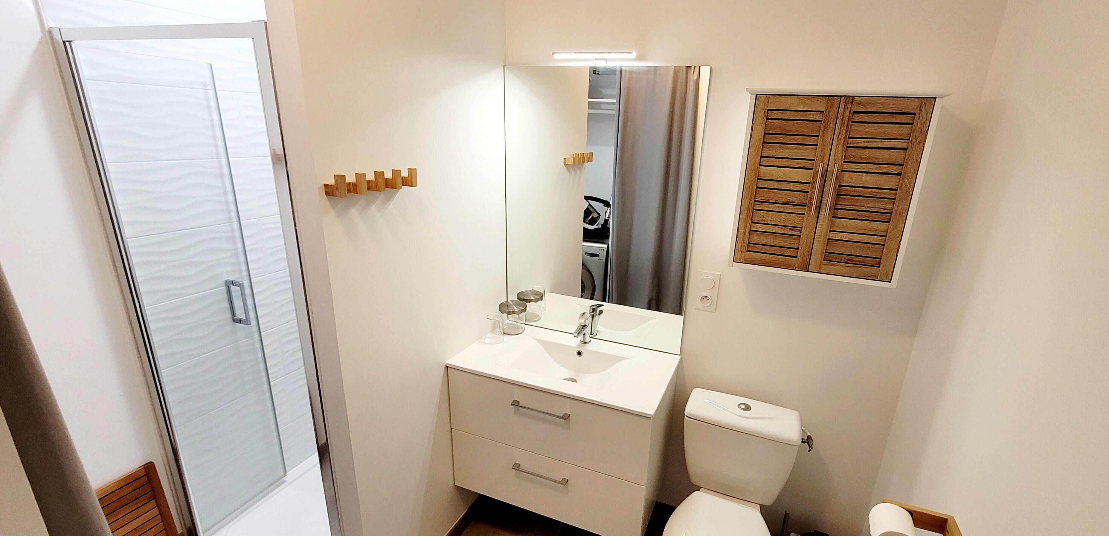 A bathroom with a glass shower door, a white sink with a mirror above it, a wooden cabinet, and a toilet.