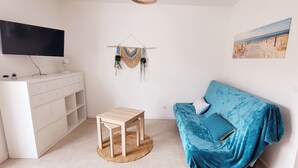 Et værelse med et fladskærms-tv, et hvidt opbevaringsskab, et lille træbord, en blå sofa og strandrelateret vægkunst.