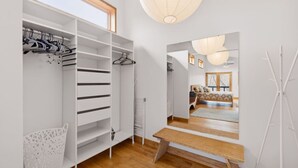 Ein modernes Interieur mit begehbarem Kleiderschrank, einer hölzernen Bank und Blick auf ein Schlafzimmer mit Bett und Fenster.