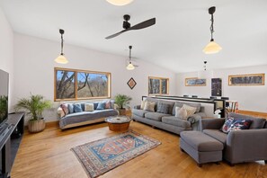 Ein geräumiges Wohnzimmer mit großem Fenster, Deckenventilator und Flachbildfernseher.