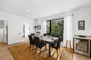 A modern dining area with a wooden table, black chairs, and a view of trees through large windows.