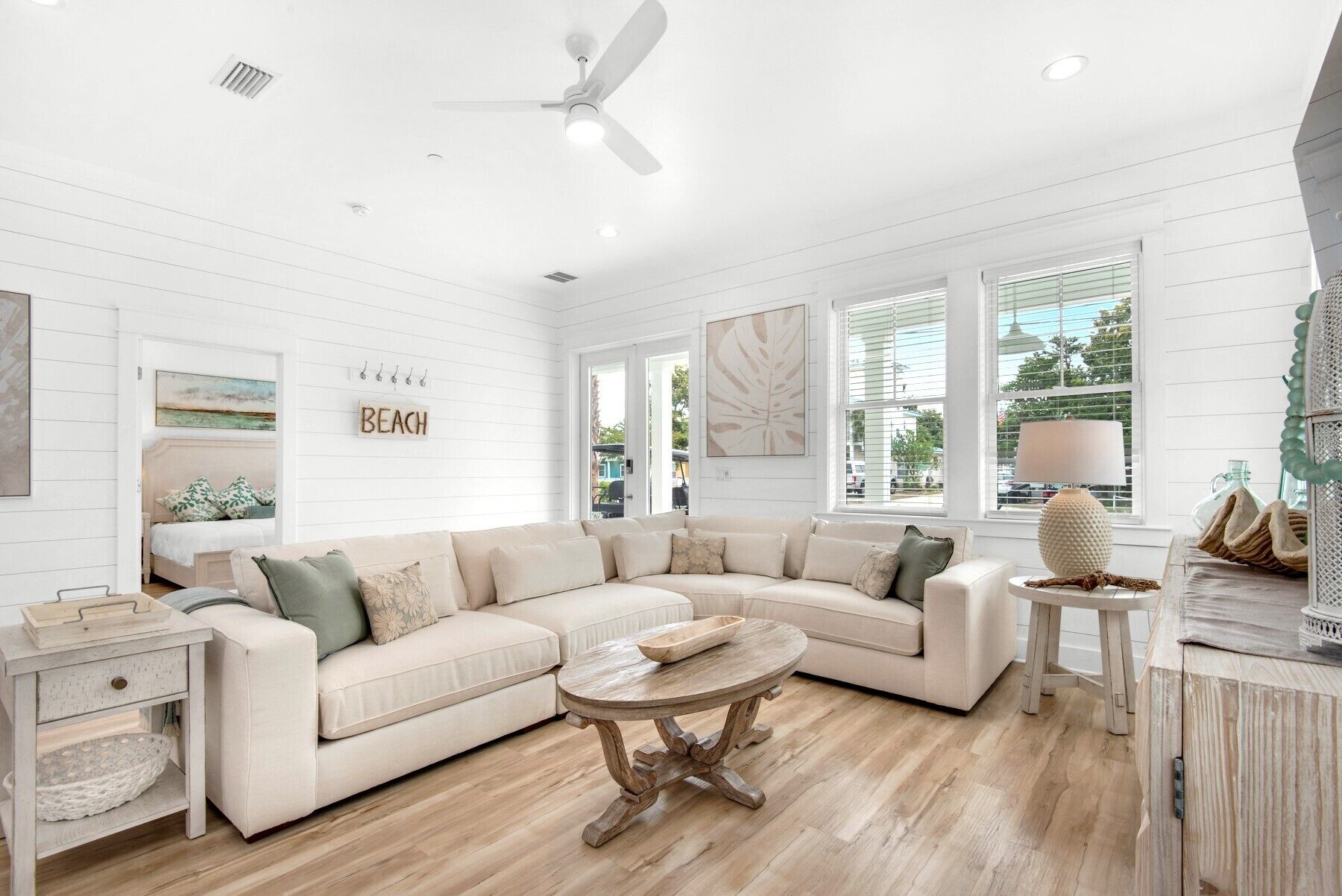 A spacious living room with a large L-shaped sectional sofa, a round wooden coffee table, and a ceiling fan.