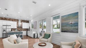 A spacious living room with a large window, a kitchen with white cabinets, and a dining area. - Windsong! New! Sleeps 19! Beach! (Destin)