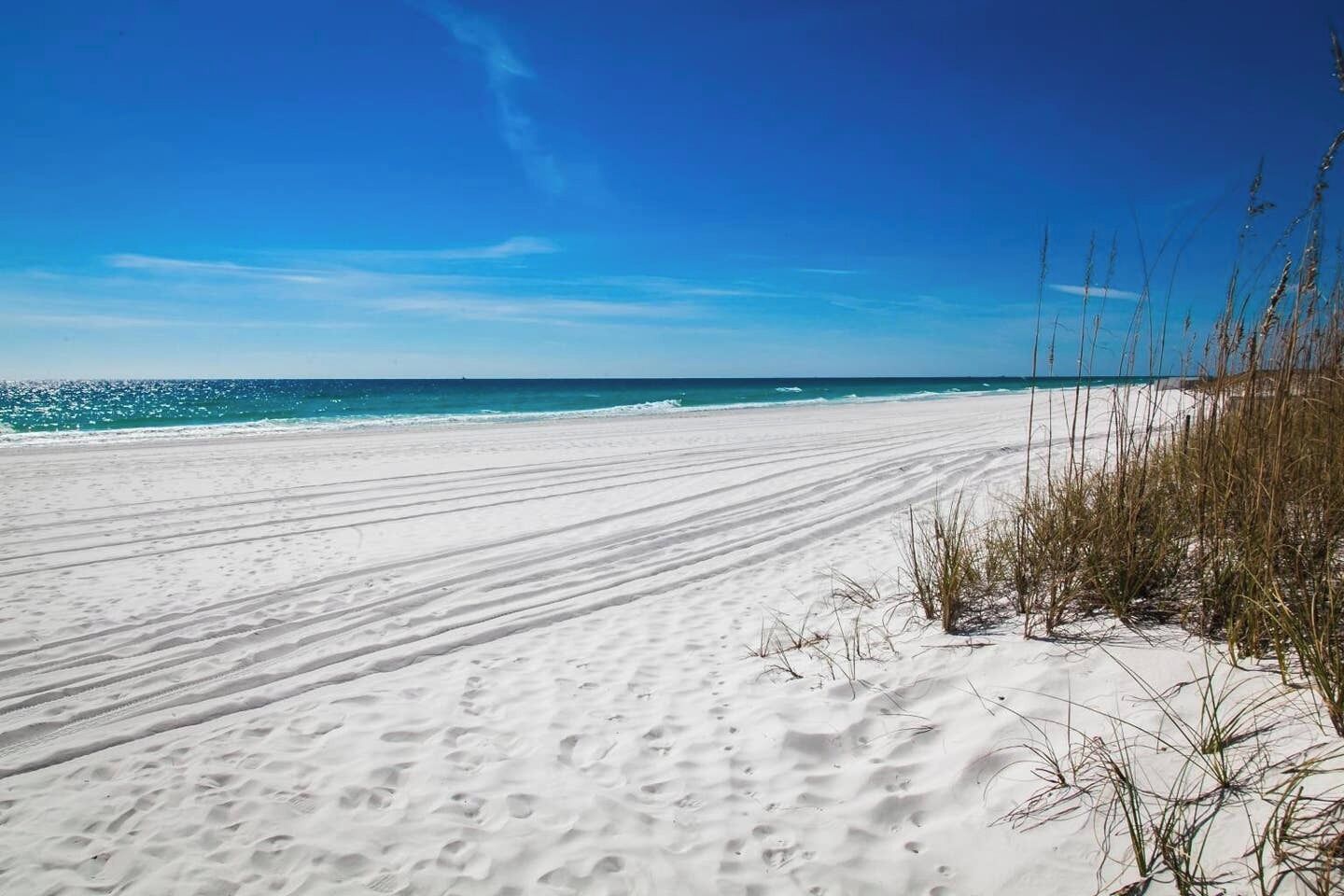 A beach with white sand and clear blue water.