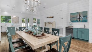 A spacious kitchen with a wooden dining table, teal chairs, and a large chandelier. - Windsong! New! Sleeps 19! Beach! (Destin)