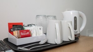 Un plateau avec une boîte de biscuits, une cuillère, deux tasses blanches et une bouilloire électrique blanche.