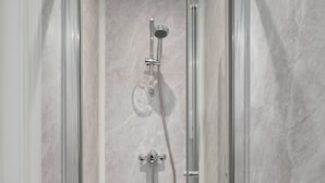 Une douche entièrementClose avec une pomme de douche à main et une pomme de douche fixe, le tout installé devant un mur de marbre.