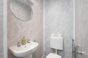 Un baño con un lavamanos blanco, un espejo redondo y un inodoro.