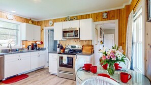 A kitchen with white cabinets, a microwave, an oven, and a dining area with a table and chairs.