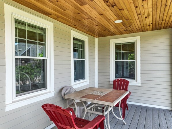 A covered porch with a table and chairs, large windows, and a wooden ceiling.