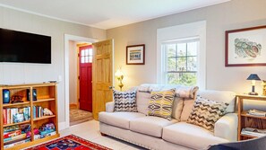 A living room with a sofa, a bookshelf, a TV, and a door leading to another room.