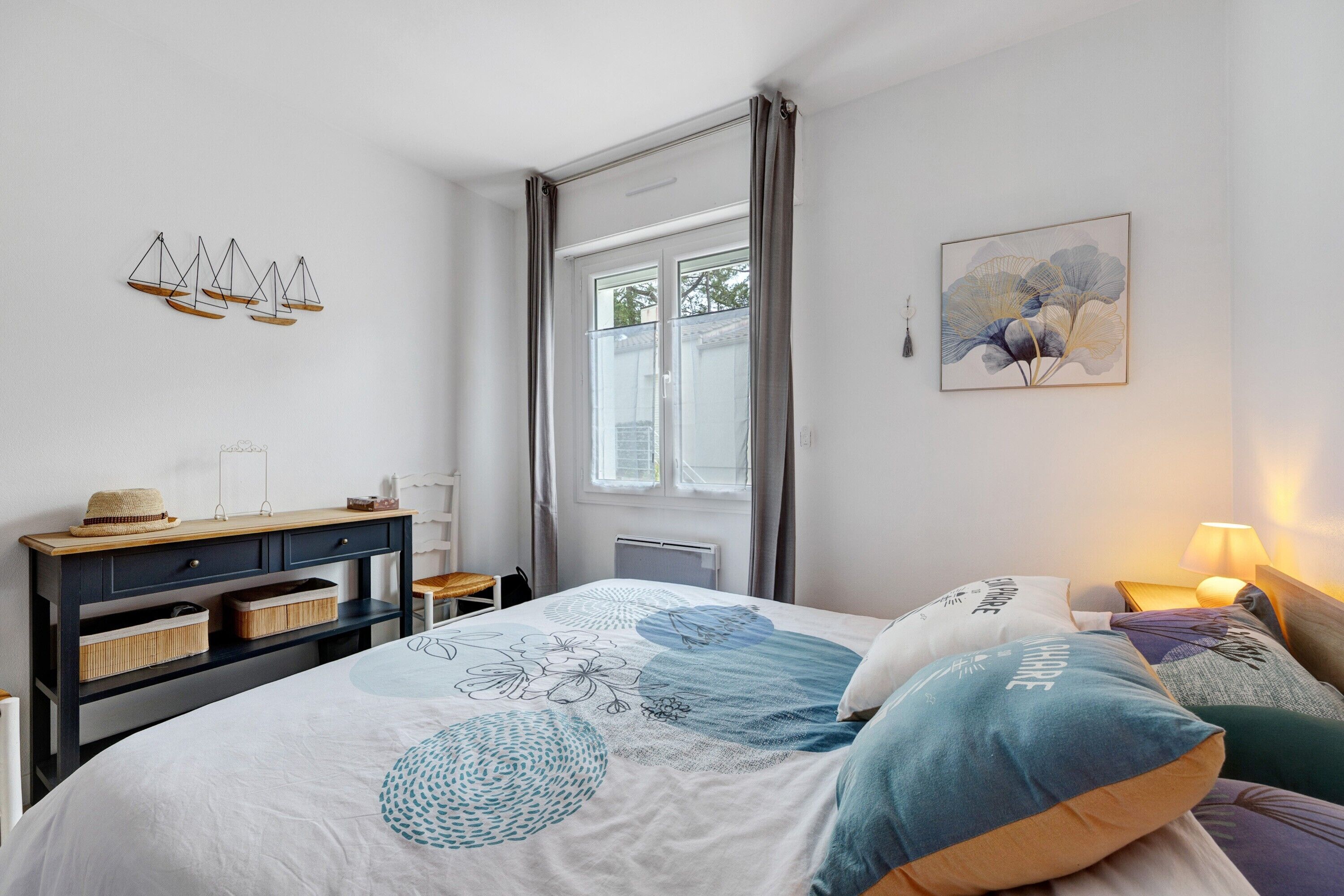 A bedroom with a bed, bedside tables, a dresser, a window, and a wall art piece.