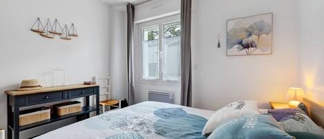 A bedroom with a bed, bedside tables, a dresser, a window, and a wall art piece.