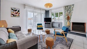 A living room with a sofa, chairs, a TV, a fireplace, and a large window. - Villa des Mahonies just 200m from the beach (La Tranche-sur-Mer)