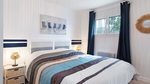 A neatly arranged bedroom with a bed, bedside lamps, a wall-mounted artwork, a window with curtains, and a decorative wall piece. - Villa des Mahonies just 200m from the beach (La Tranche-sur-Mer)