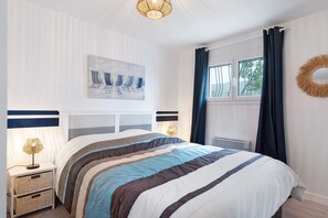 A neatly arranged bedroom with a bed, bedside lamps, a wall-mounted artwork, a window with curtains, and a decorative wall piece. - Villa des Mahonies just 200m from the beach (La Tranche-sur-Mer)