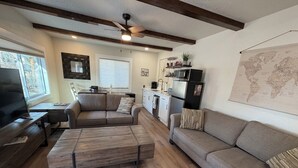 A modern living room with a wooden floor, a sofa, a coffee table, a TV, and a ceiling fan. - Welcome to the Sundancer @ the Little Littleton Village (Littleton)