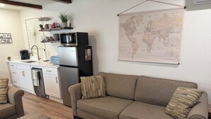 A living room with a sofa, coffee table, and a kitchen area with appliances. - Welcome to the Sundancer @ the Little Littleton Village (Littleton)