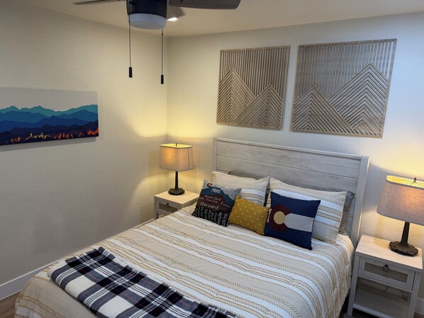 A bedroom with a bed, two nightstands, a ceiling fan, and wall art.